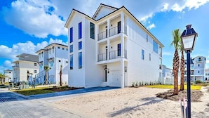 A multi-story residential building with balconies, a paved walkway, and palm trees.
