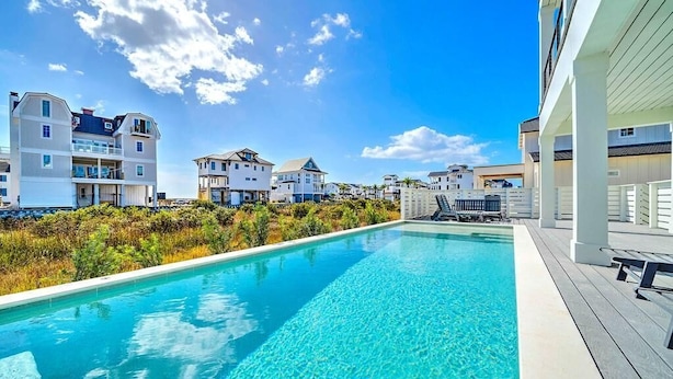 A swimming pool with clear blue water, surrounded by buildings with balconies and a wooden deck.