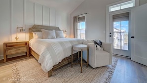 A bedroom with a large bed, a nightstand, a chair, and a view of the outside.