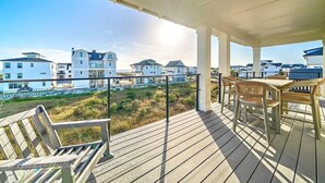 A wooden deck with outdoor furniture, overlooking a beach and residential buildings.
