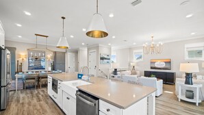 Une cuisine moderne dotée d’un îlot central, d’appareils électroménagers intégrés et de luminaires suspendus.
