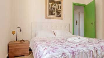 A bedroom with a bed, a nightstand, a framed artwork, and a green door.