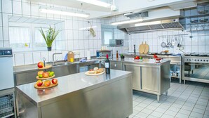 A modern kitchen with stainless steel appliances, a central island with fruits, and a microwave above the sink. - Winery Retreat in Germany With Wine Cellar (Sankt Goar)
