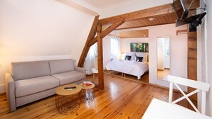 A cozy loft bedroom with a wooden ceiling, a bed, a sofa, and a TV mounted on the wall. - Winery Retreat in Germany With Wine Cellar (Sankt Goar)