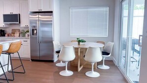 Eine moderne Küche mit weißen Schränken, einem Edelstahlkühlschrank und einem Essbereich mit weißen Stühlen und einem Holztisch.