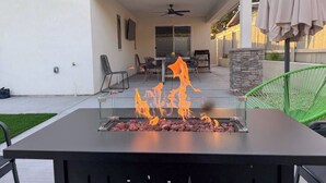 Eine Terrrasse im Freien mit Feuerstelle, Deckenventilator und Essbereich mit Stühlen und Tisch.