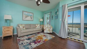 A living room with a sofa, a patterned rug, a wooden side table, a lamp, and a beach view through a sliding door. - Grand Caribbean 206 Fun in the Sun! (Orange Beach)