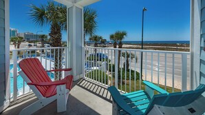 A balcony with two red and two blue Adirondack chairs, a pool, and a view of the beach and ocean. - Grand Caribbean 206 Fun in the Sun! (Orange Beach)