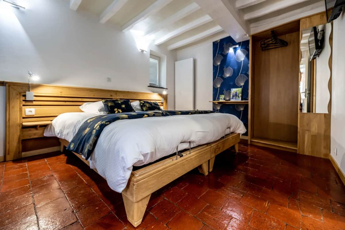 Une chambre à coucher avec un lit en bois, une table de chevet, une commode et un mur bleu orné d’un ventilateur.