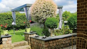 Een terras met een stenen muur, plantenpotten en een boom.