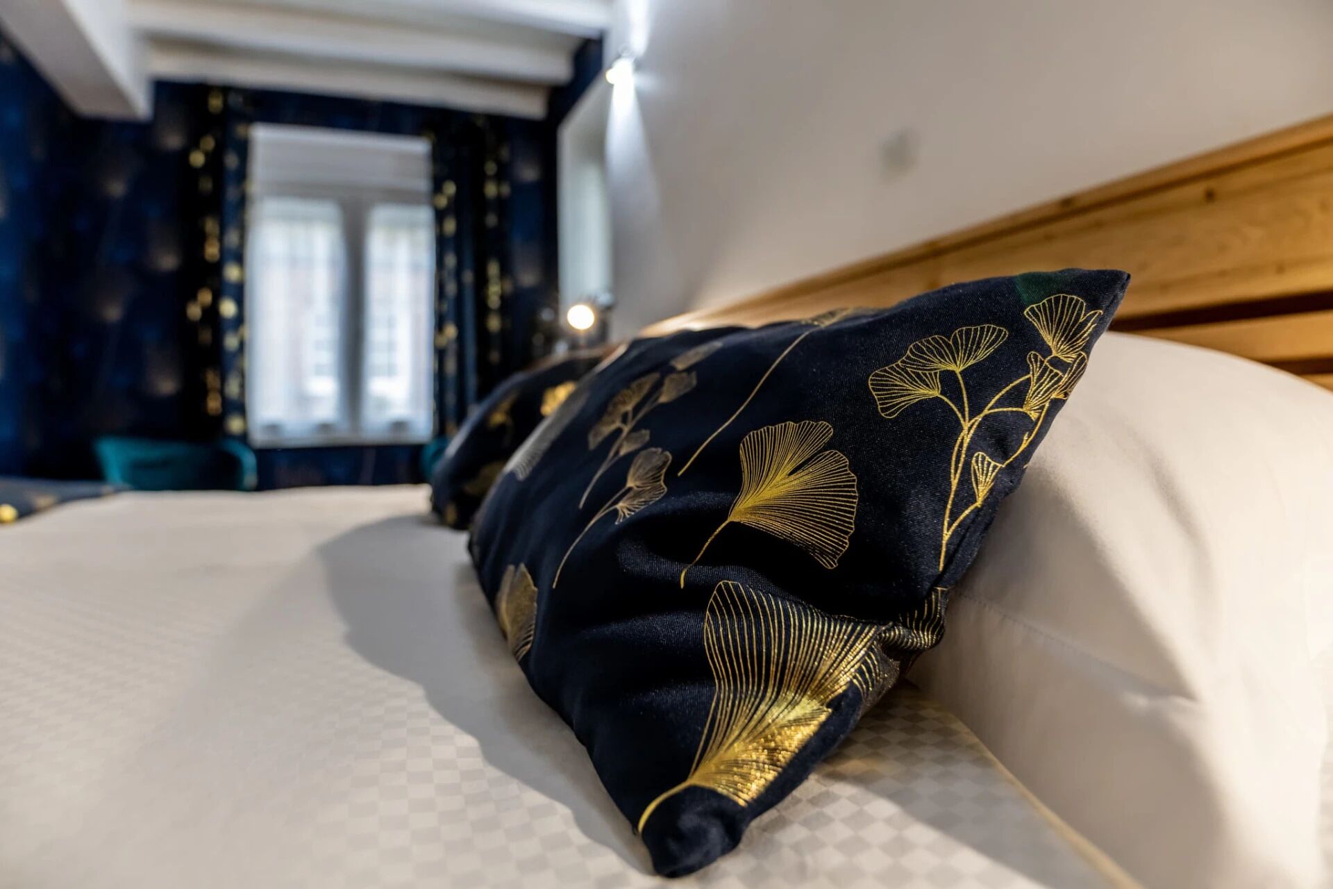 A bed with a dark blue pillow featuring golden floral embroidery.