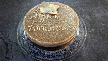 A round cake with "Joyeux Anniversaire" written on top, placed on a decorative glass plate.