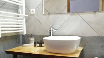 A modern bathroom with a large white sink, a wooden vanity, a towel rack, and a small shelf with toiletries.