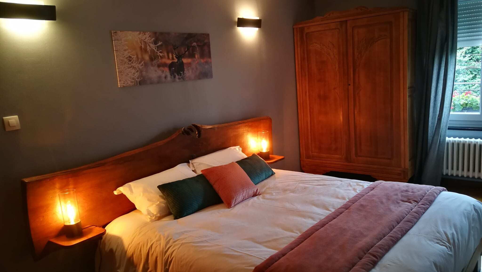 Un llit ben arreglat amb un panell frontal de fusta, dues làmpades de nit i un quadre a la paret.