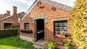 Een huis van baksteen met een schilddak, een zichtbare schoorsteen en een kleine voortuin met planten in potten.