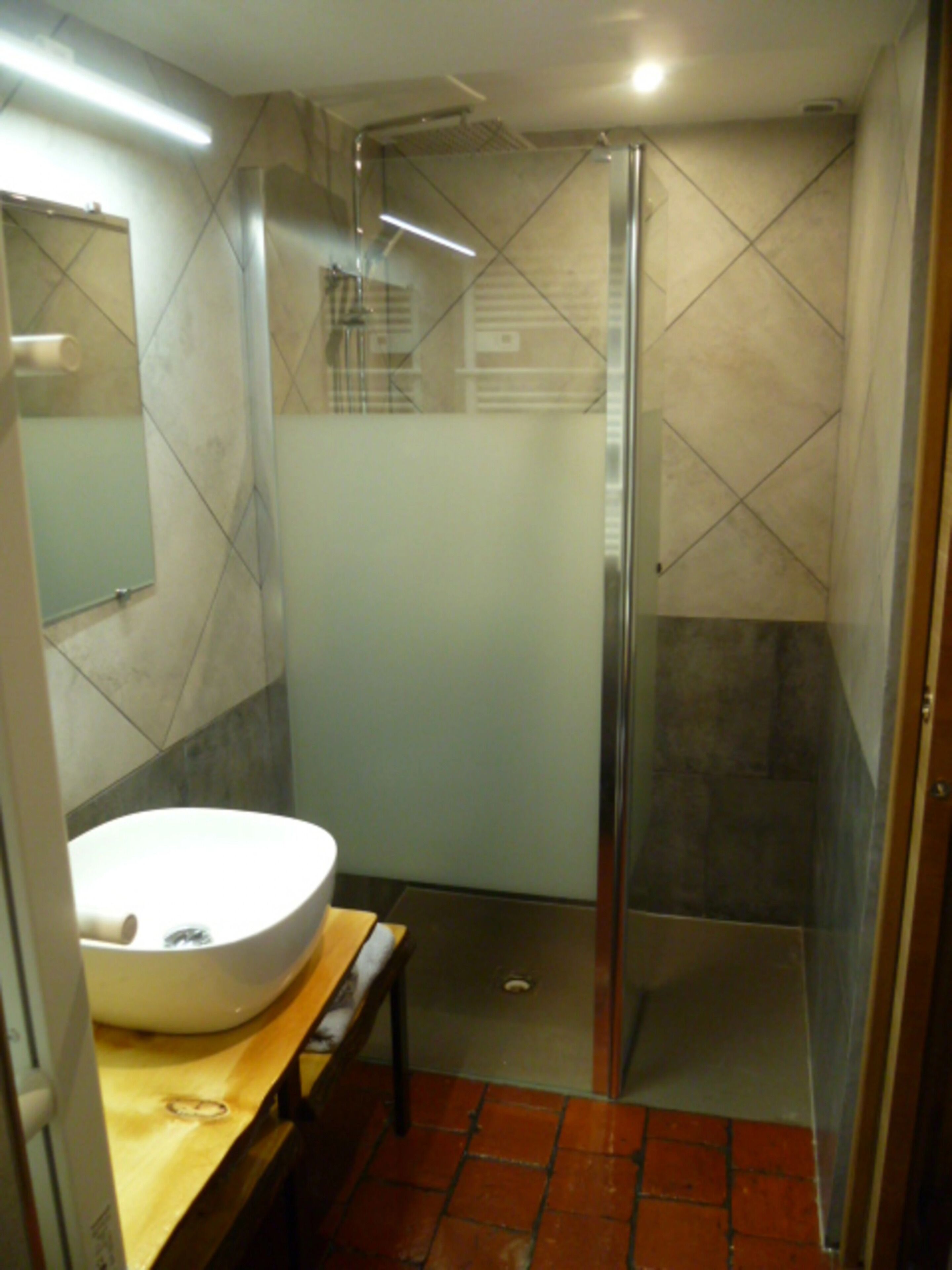 A bathroom with a large white sink, a mirror, a shower with a glass door, and tiled walls.