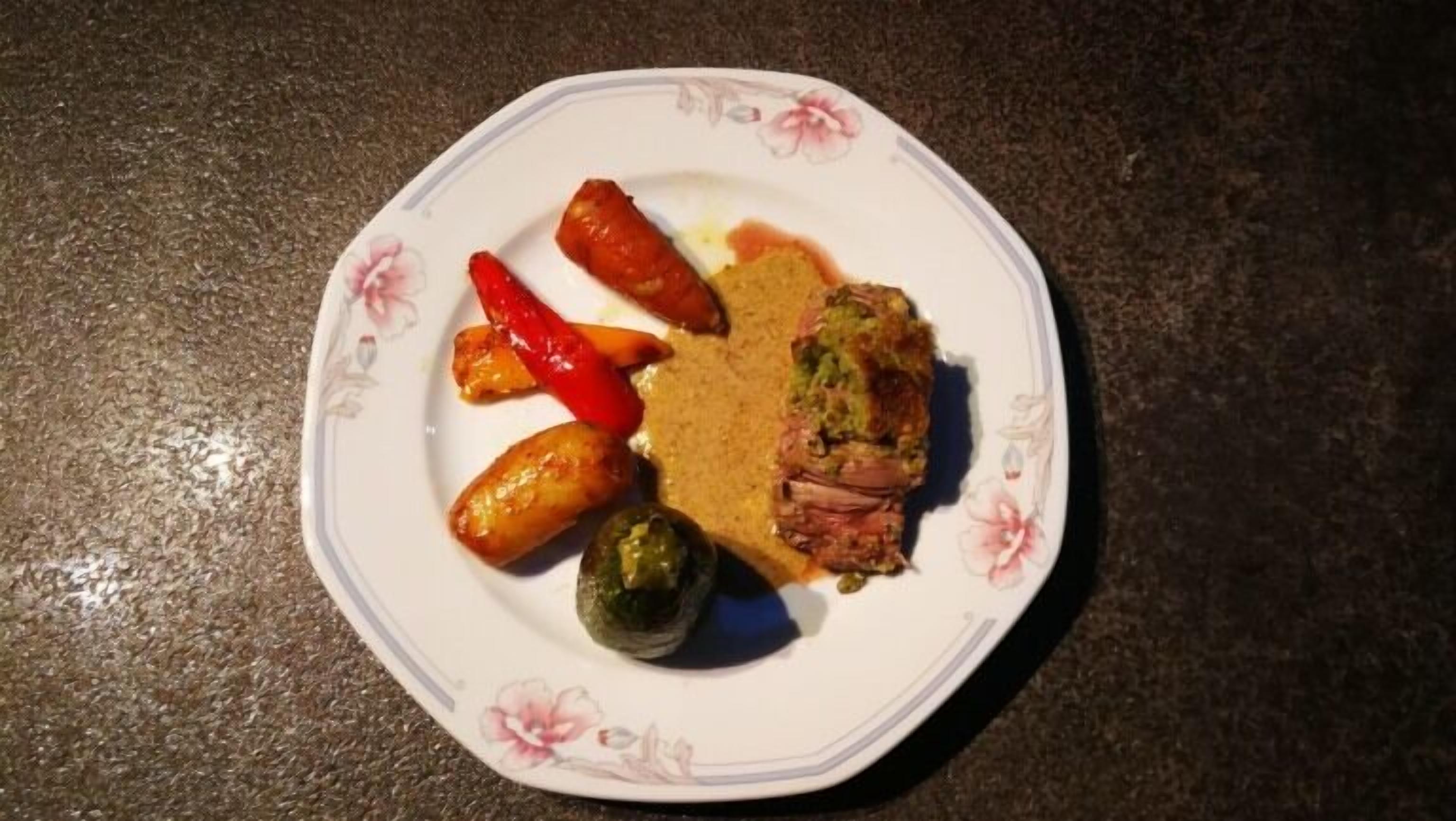 Une assiette ornée de motifs floraux, sur laquelle on trouve un morceau de viande, deux poivrons rouges et deux poivrons verts.