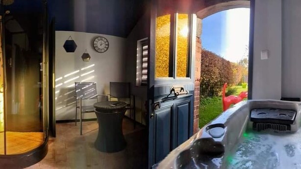 Een badkamer met een douchecabine van glas, een bad met groene verlichting, een klok aan de muur en een raam met zonwering.