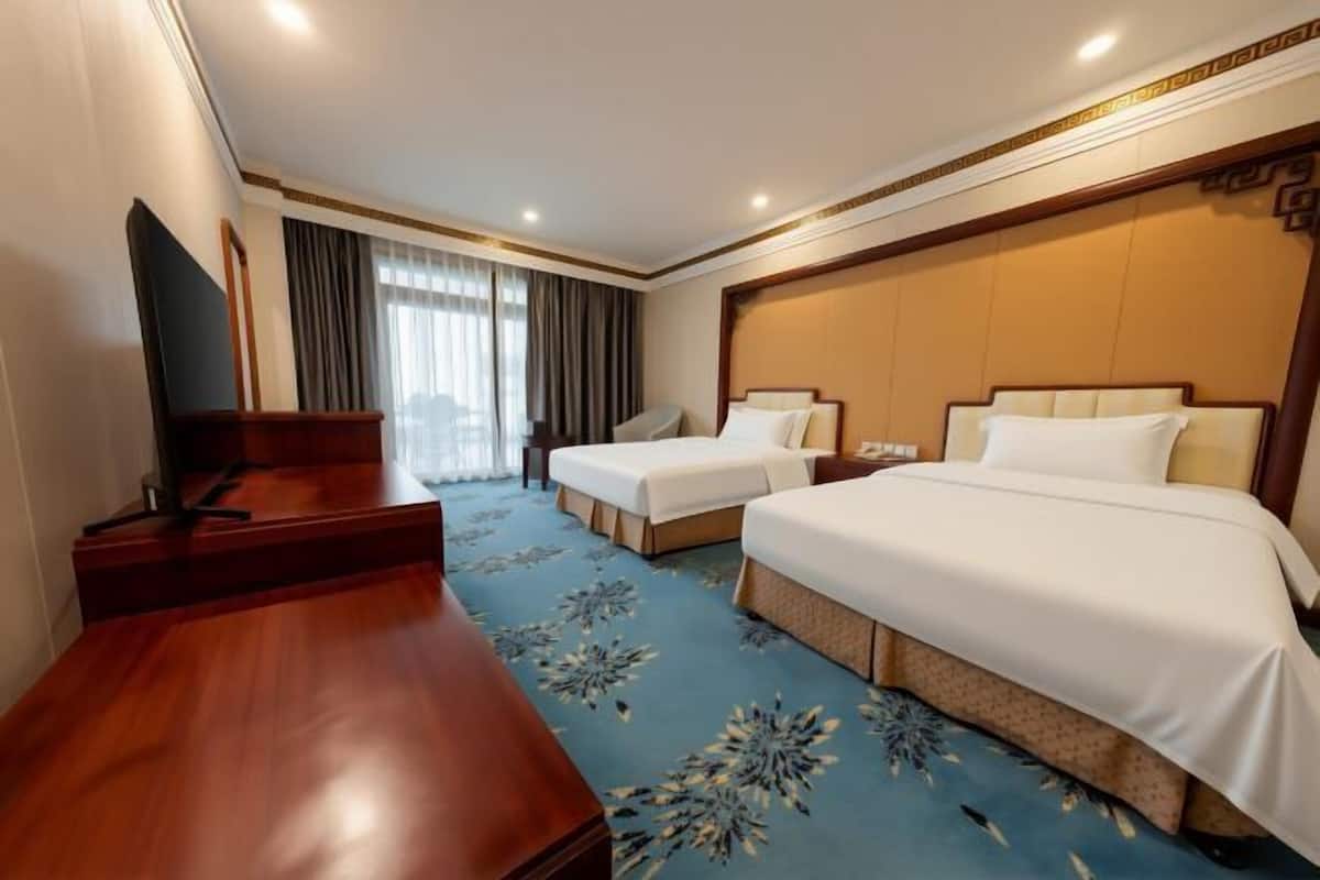 A hotel room with two beds, a desk, and a TV.