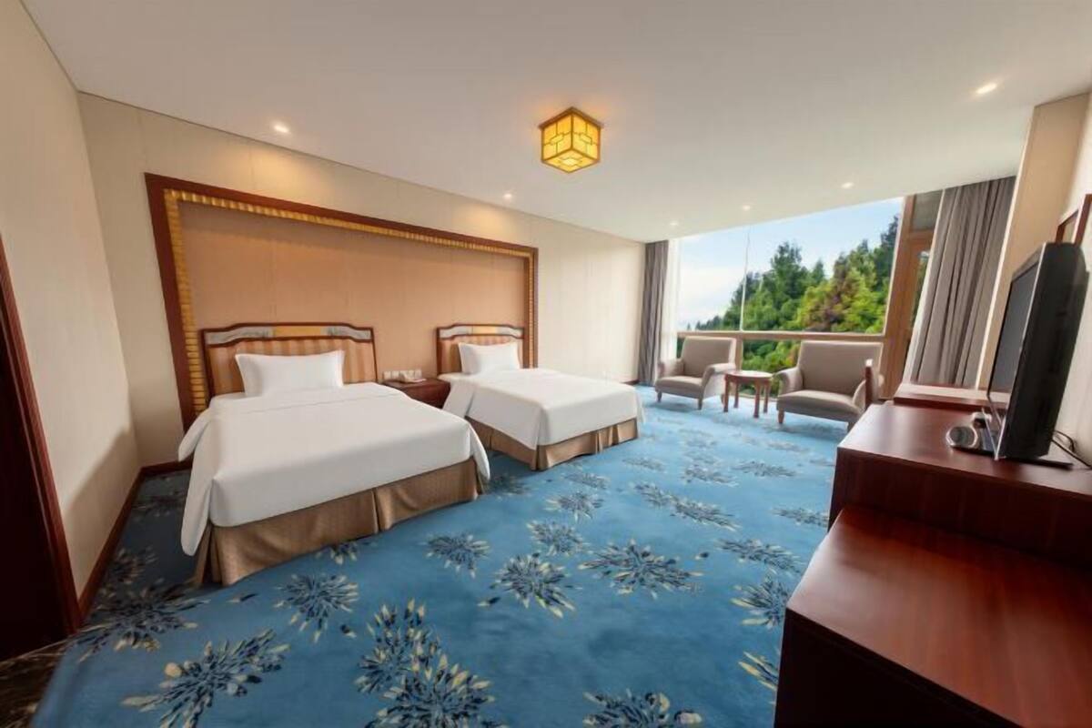 A hotel room with two beds, a desk, a chair, and a balcony with a view.