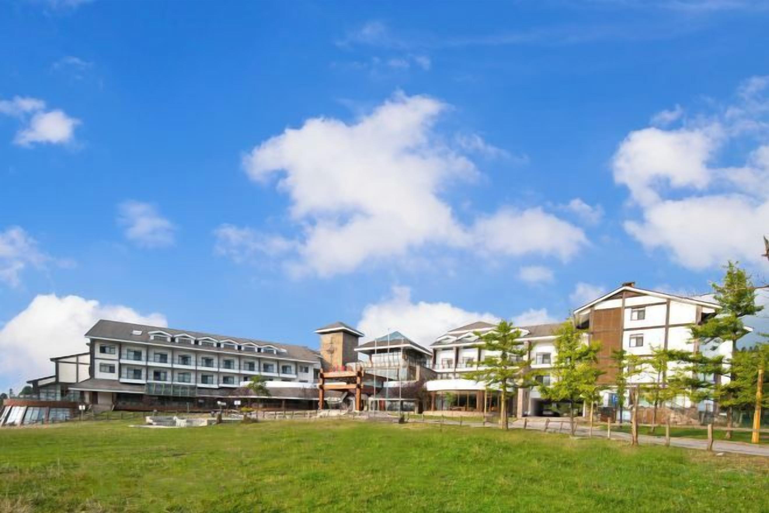 A hotel with multiple buildings, a grassy area in front, and a clear sky.
