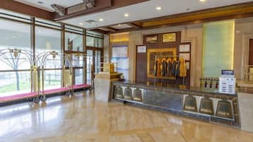 A hotel reception area with a marble floor, a reception desk, a coat rack, and a window with a view.