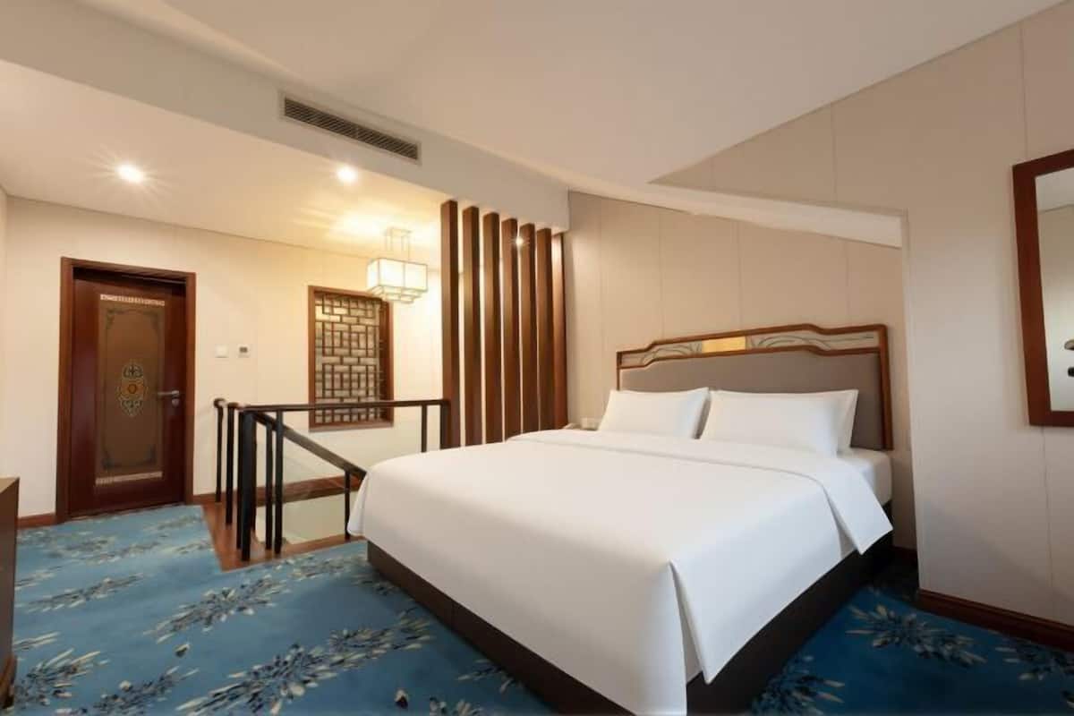 A hotel room with a bed, a desk, a chair, a door, and a wall-mounted mirror.