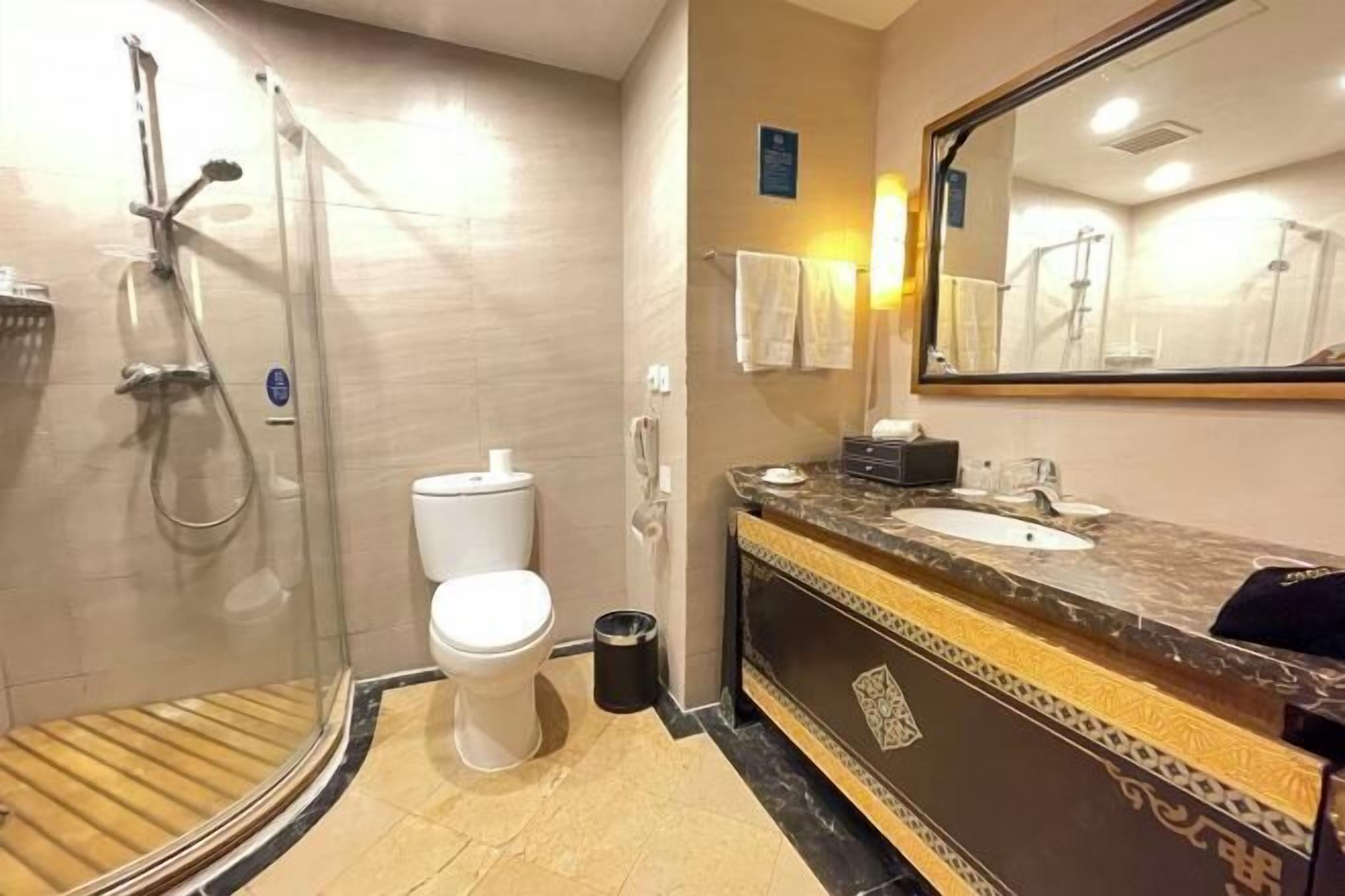 A bathroom with a glass-enclosed shower, a toilet, a sink with a marble countertop, and a mirror.
