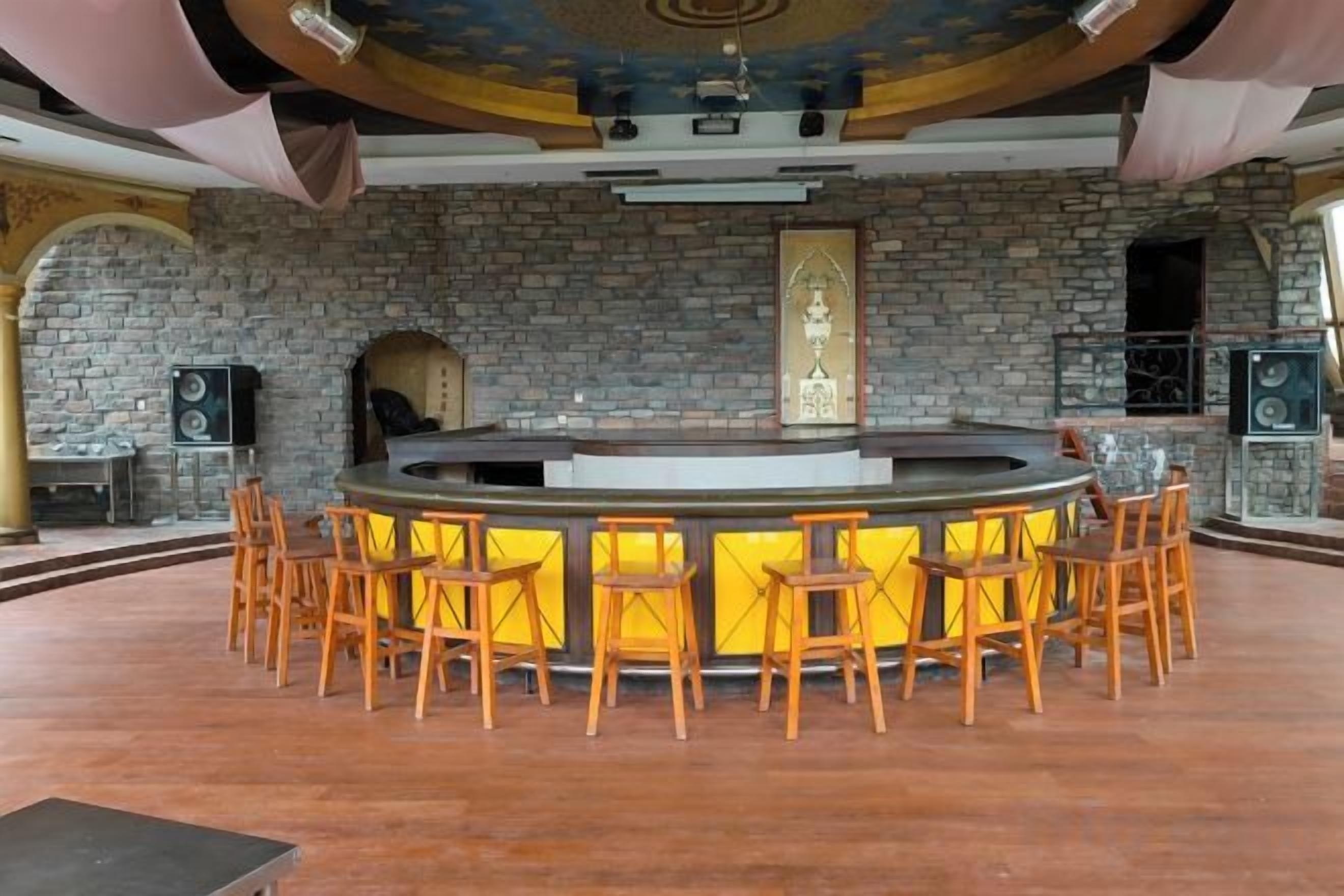 A bar area with a stone wall backdrop, a central bar counter, and wooden bar stools.