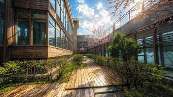 A modern building with large windows, a wooden deck, and a pathway surrounded by greenery.