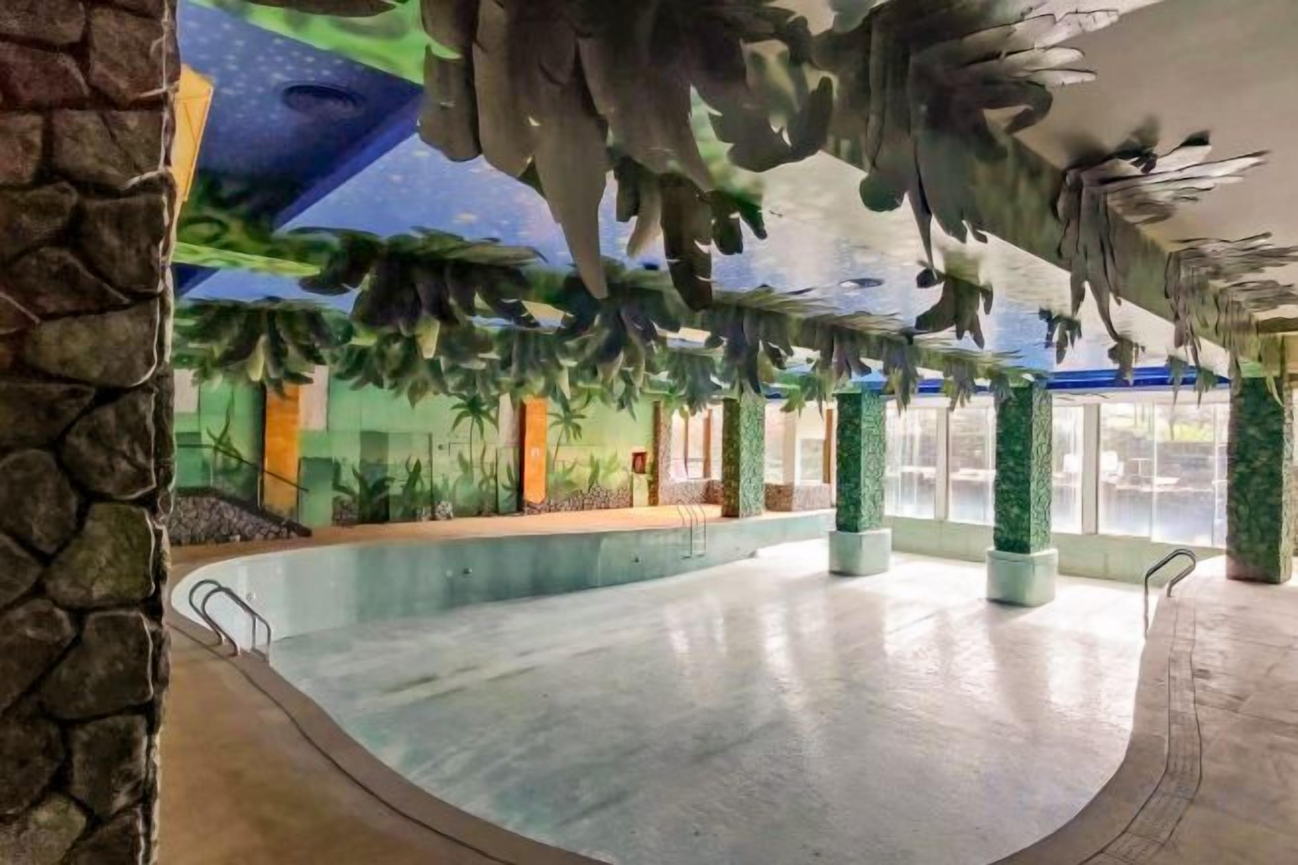 Piscina com borda curva, rodeada por colunas e teto com detalhes em forma de folhas.
