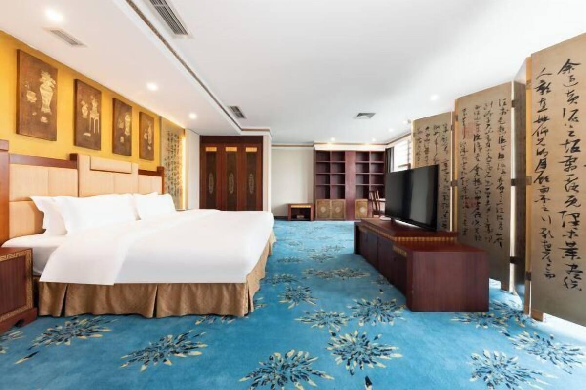 A hotel room with a large bed, a TV, and a bookshelf.