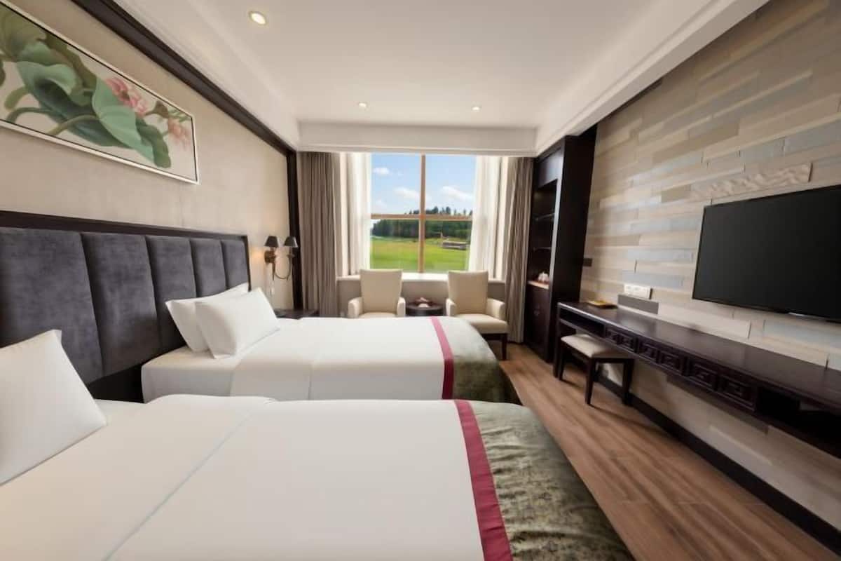 A hotel room with two beds, a TV, a desk, and a large window with a view.