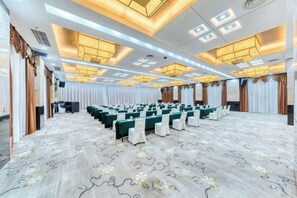 Un salón de conferencias con filas de mesas y sillas, una alfombra estampada e iluminación empotrada en el techo.