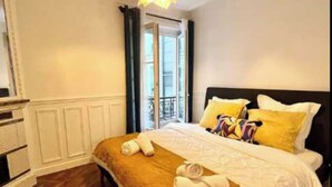 A hotel room with a bed, a wooden floor, a window with curtains, and a ceiling light fixture. - Elegant Apartement - AC 2br-6p- Palais des Congres (Paris)
