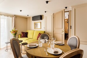 A dining area with a round table set for four, a sofa with cushions, a vase of flowers, and a television mounted on the wall.