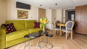A living room with a green sofa, two round tables, and a dining area with wooden chairs. - Merveil - Luxury Suite - Marais - Turenne (Paris)