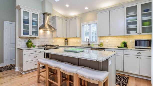 Una cocina moderna con armarios blancos, una isla central con taburetes y un tragaluz.