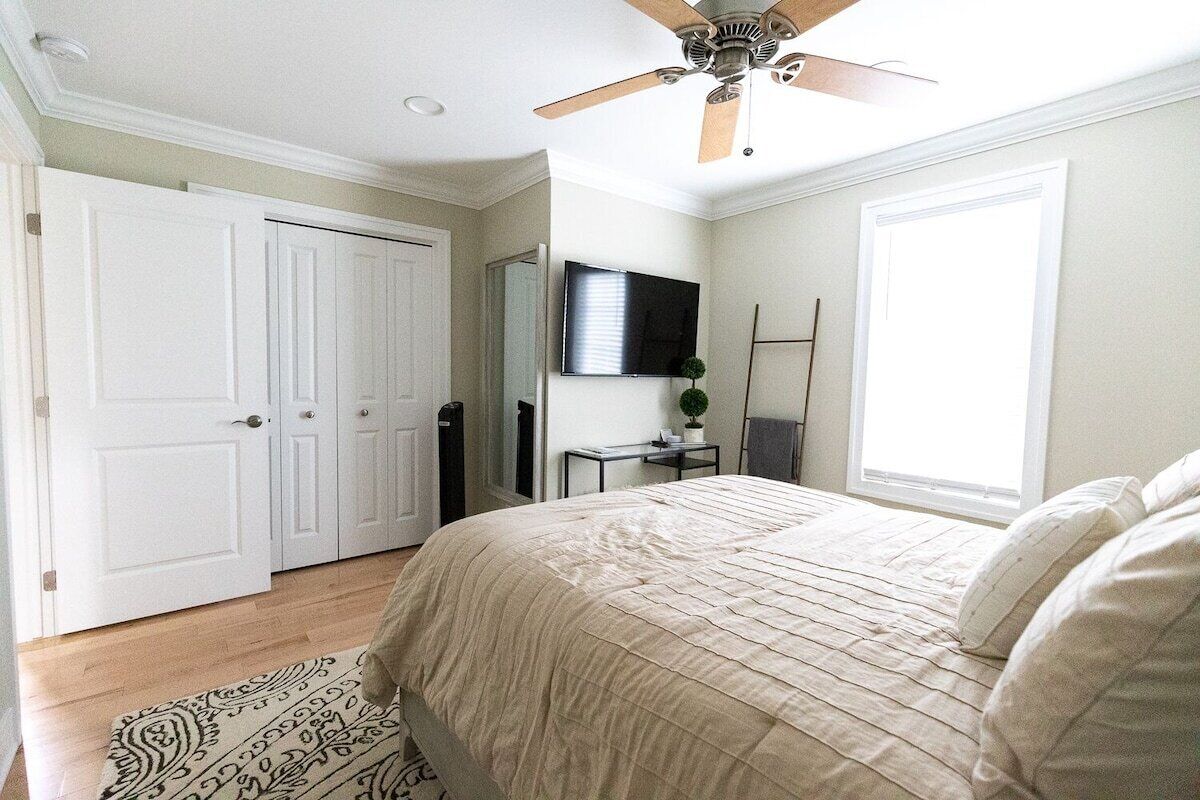 A bedroom with a bed, a ceiling fan, a TV, and a window.