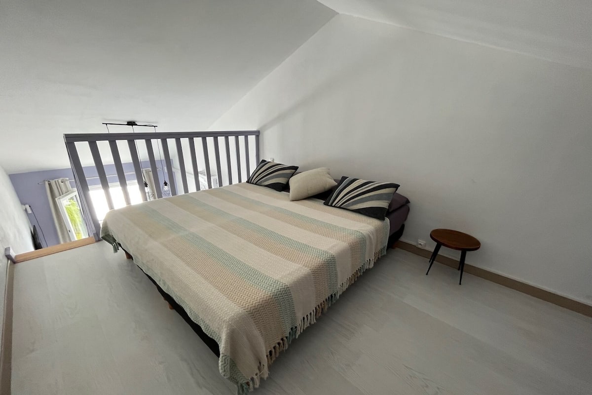 A bedroom with a large bed, a small table, and a balcony with a railing.