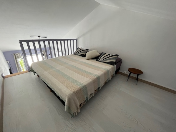 A bedroom with a large bed, a small table, and a balcony with a railing.