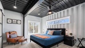 A bedroom with a bed, a chair, a nightstand, and a window.