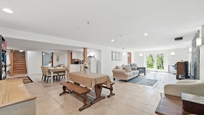 Amplia sala de estar con una mesa de comedor, un sofá y un banco. Se ve una escalera que lleva a otro nivel, y un televisor al fondo.