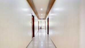 A long, narrow hallway with a shiny tiled floor and wooden doors on both sides. - Stylish Stays at MG Road Near Commercial Street (Bengaluru)