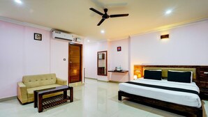 A hotel room with a bed, a sofa, a coffee table, an air conditioning unit, a ceiling fan, a mirror, and a small shelf with toiletries. - Stylish Stays at MG Road Near Commercial Street (Bengaluru)