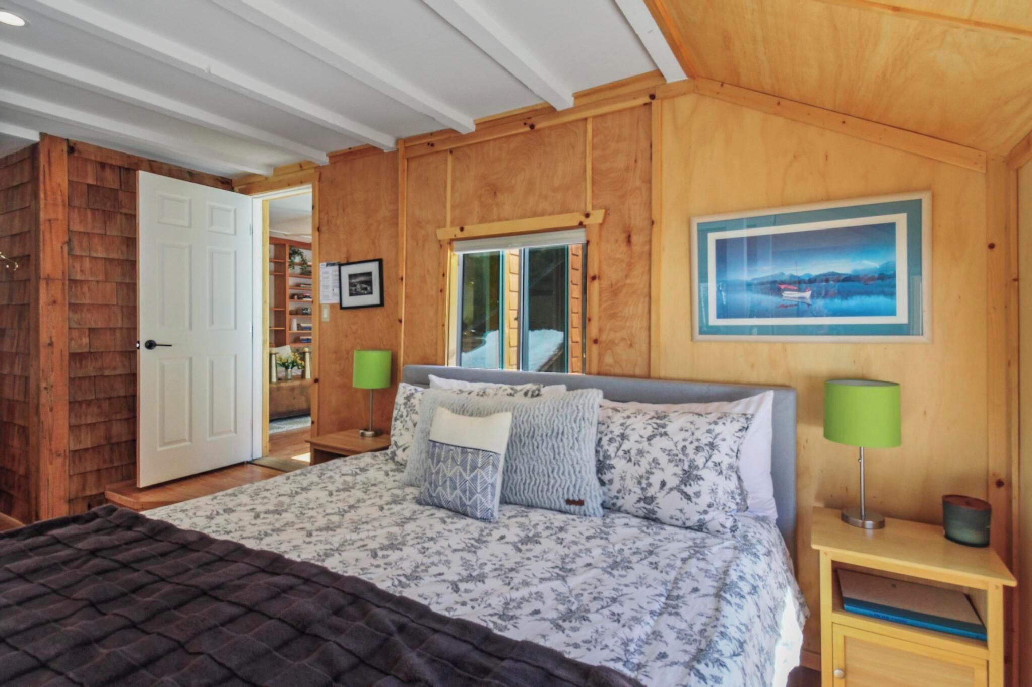 Un dormitorio con paneles de madera, una cama, una mesita de noche, una lámpara verde y un cuadro enmarcado en la pared.