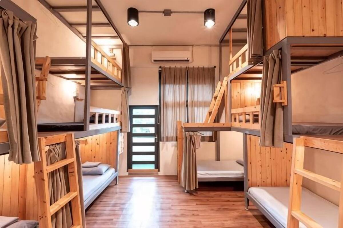 A bunk bed room with wooden walls and floors, a central air conditioning unit, and a window with curtains.
