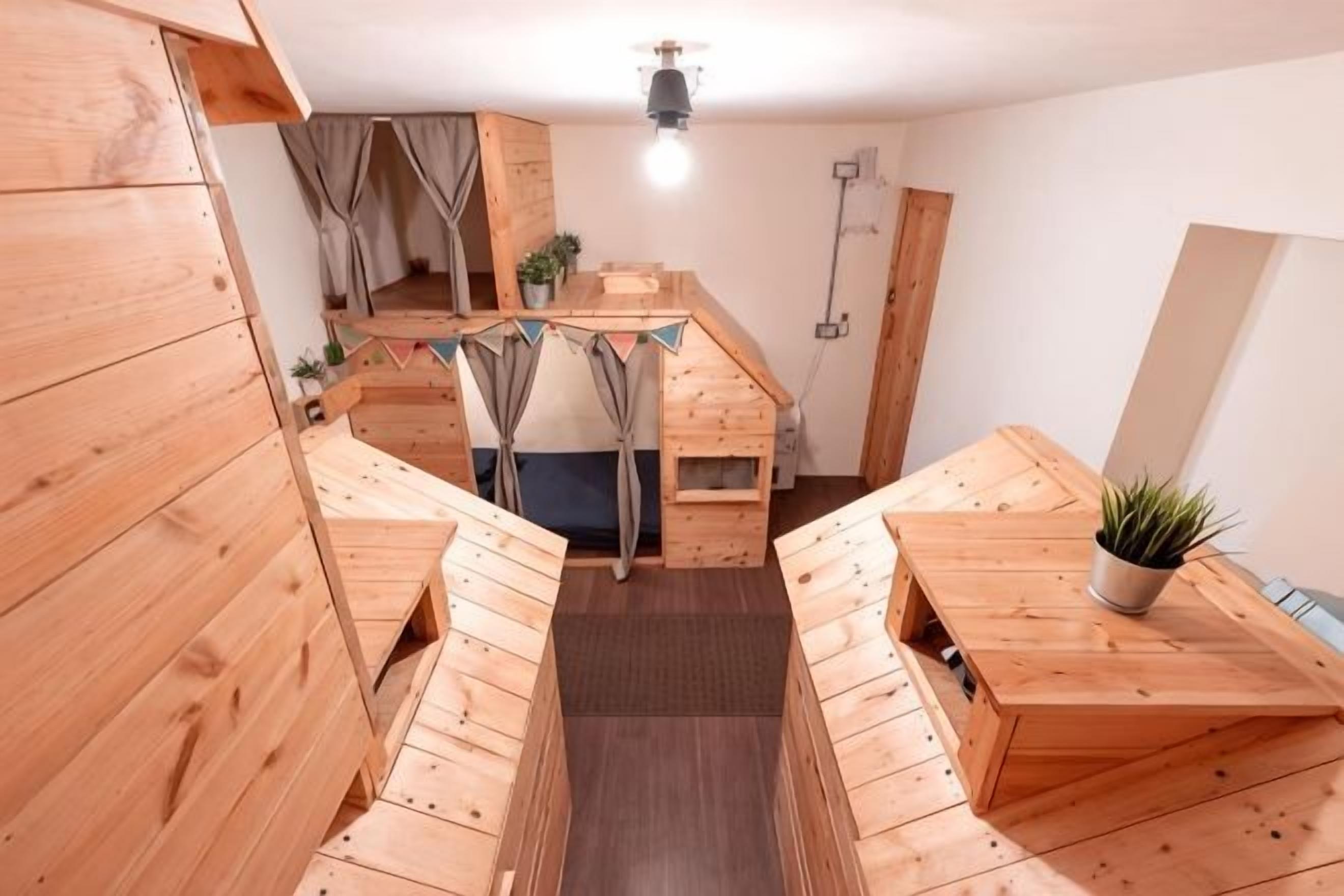 A compact, multi-level wooden room with a loft bed, a small dining area, and a potted plant.