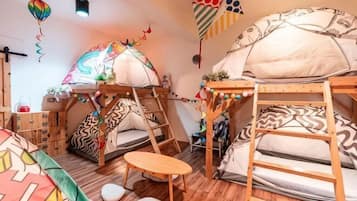 A room with bunk beds, a small table, and a tent-like structure.