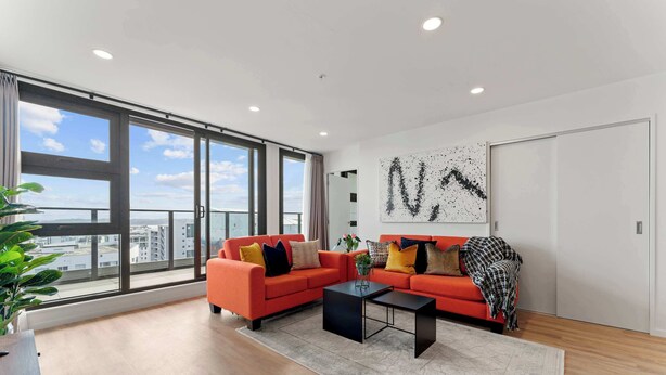 A modern living room with a large window, a red sofa, a black coffee table, and a city view. - Penthouse 3BR & 2Bath-Skytower View-Pool, Parking (Auckland)